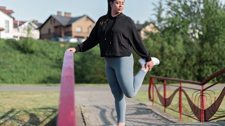 Young woman in activewear stretching on a red railing outdoors.