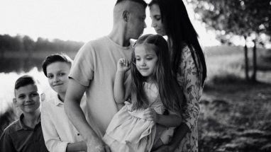 A serene black and white portrait of a family standing by a lake.