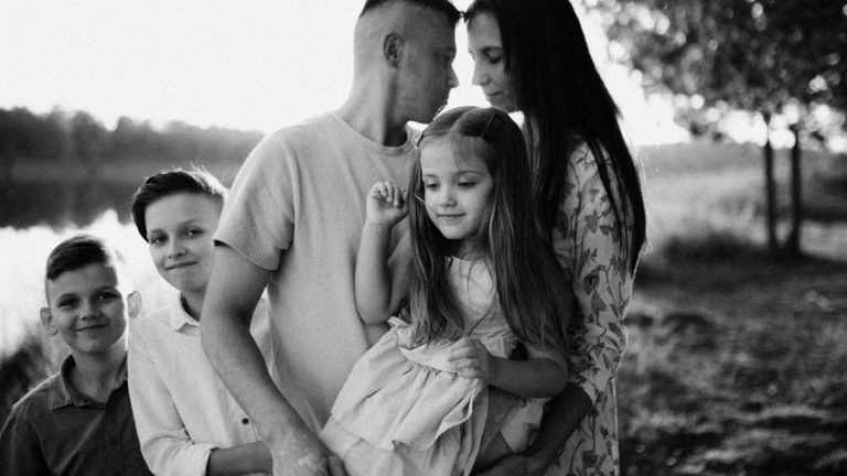 A serene black and white portrait of a family standing by a lake.