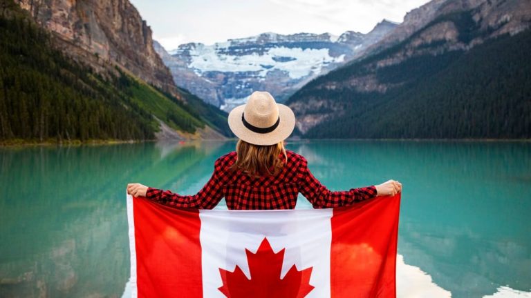 Woman holding a Canadian flag at stunning Lake Louise, Alberta, embracing nature and patriotism.